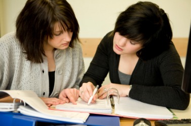 Two young women looking at a document in a binder together