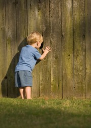 A child peeks through a hole in a fence. A child peeks through a hole in a fence.