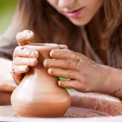 She is working in plastic arts by creating a three dimensional clay pot. She is working in plastic arts by creating a three dimensional clay pot.