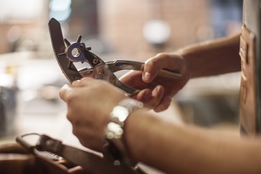The craftsman uses a punch to put holes in a leather belt. The craftsman uses a punch to put holes in a leather belt.