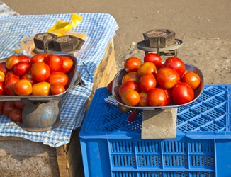 The produce vendor uses a seer to calculate the weight of tomatoes at a market in Ernakulam, India. The produce vendor uses a seer to calculate the weight of tomatoes at a market in Ernakulam, India.