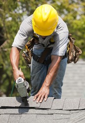 A worker is nailing shingles on the roof of a house. A worker is nailing shingles on the roof of a house.
