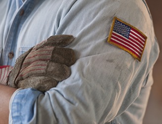 The worker has a patch of the American flag sewn on the sleeve of his shirt. The worker has a patch of the American flag sewn on the sleeve of his shirt.
