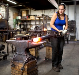 The metalsmith is turning a red hot metal rod on a workshop anvil. The metalsmith is turning a red hot metal rod on a workshop anvil.