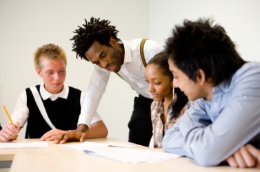 A teacher helping a student while her classmates look on. A teacher helping a student while her classmates look on.