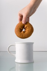 A hand about to dip a donut into a cup of coffee. A hand about to dip a donut into a cup of coffee.