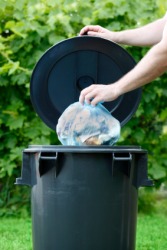 A woman dumps trash into a trash can. A woman dumps trash into a trash can.