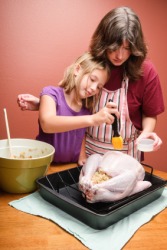 A child helping her mother to baste a turkey. A child helping her mother to baste a turkey.
