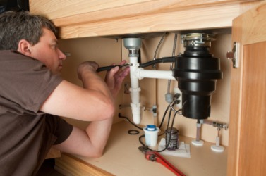A man works on the plumbing under a sink. A man works on the plumbing under a sink.