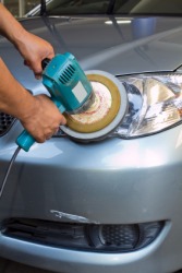 A man burnishes the lights of his car. A man burnishes the lights of his car.