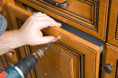 A person bores a hole in a cabinet door. A person bores a hole in a cabinet door.