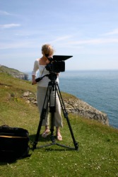 A camerawoman working on a cliff near the beach. A camerawoman working on a cliff near the beach.