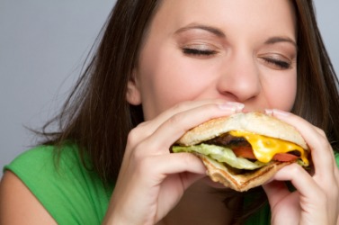 A woman consumes a hamburger. A woman consumes a hamburger.