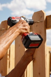 A man using a drill to build a fence. A man using a drill to build a fence.