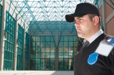 A security guard stands as sentinel in front of an office building. A security guard stands as sentinel in front of an office building.