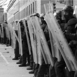 Riot police standing behind their shields Riot police standing behind their shields