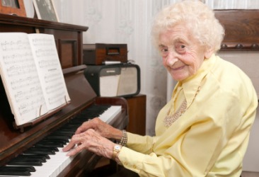 An elderly woman plays an upright piano. An elderly woman plays an upright piano.