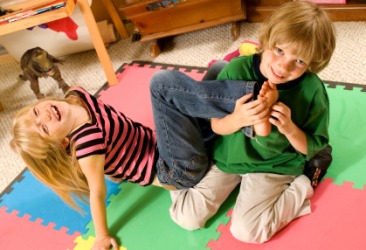 A boy tickles his sisters feet. A boy tickles his sisters feet.