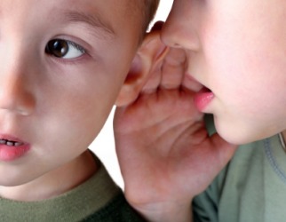 A child whispers in his friends ear. A child whispers in his friends ear.