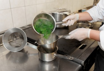 A chef blanches fresh spinach. A chef blanches fresh spinach.