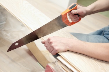 A man using a hand saw to cut wood. A man using a hand saw to cut wood.