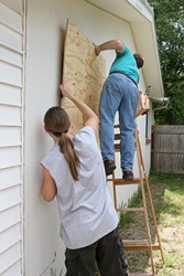 Two men putting plywood over windows in preparation of a storm. Two men putting plywood over windows in preparation of a storm.