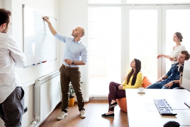 A team listening to a project manager explain a timeline for an assignment. A team listening to a project manager explain a timeline for an assignment.