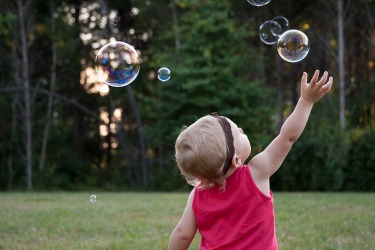 The young child protracts her arm to touch the bubbles. The young child protracts her arm to touch the bubbles.