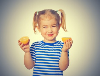 The young girl's face puckers while eating a lemon. The young girl's face puckers while eating a lemon.