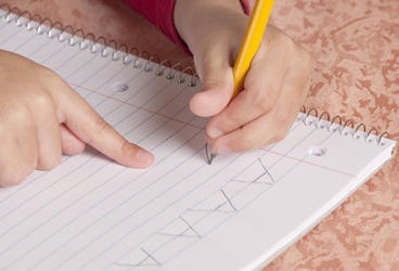 The young student is learning the alphabet by rote while also improving manual dexterity writing the letters by hand. The young student is learning the alphabet by rote while also improving manual dexterity writing the letters by hand.