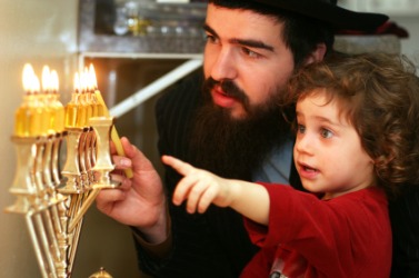 A child watches his father light the menorah to celebrate Hanukkah. A child watches his father light the menorah to celebrate Hanukkah.