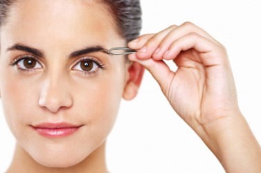 A woman uses tweezers to pluck her eyebrows. A woman uses tweezers to pluck her eyebrows.