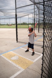 A young boy standing in a batting cage. A young boy standing in a batting cage.
