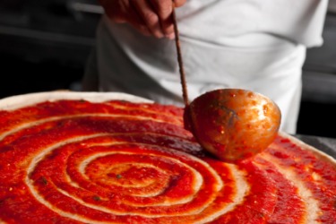 Pizza being ladled onto a pizza crust. Pizza being ladled onto a pizza crust.